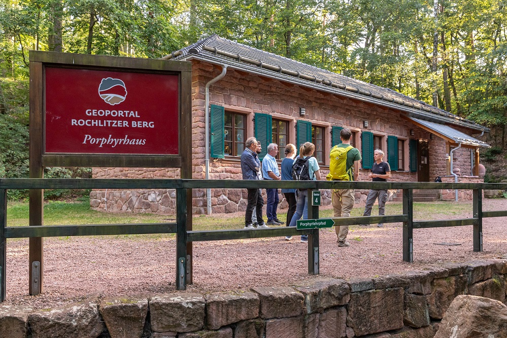 Das Porphyrhaus ist aus mit Rochlitzer Porphyr gebaut und steht im Wald. Vor dem Haus ist eine geführte Wandergruppe.